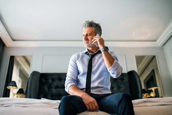 Mature businessman with smartphone in a hotel room. Handsome man making a phone call.