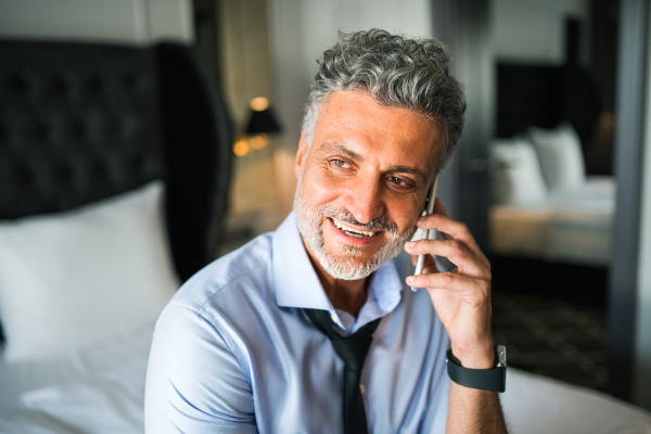 Mature businessman with smartphone in a hotel room. Handsome man making a phone call.