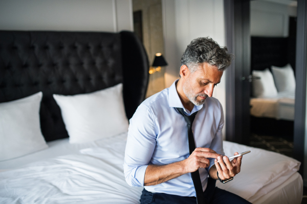 Mature businessman with smartphone in a hotel room. Handsome man text messaging.