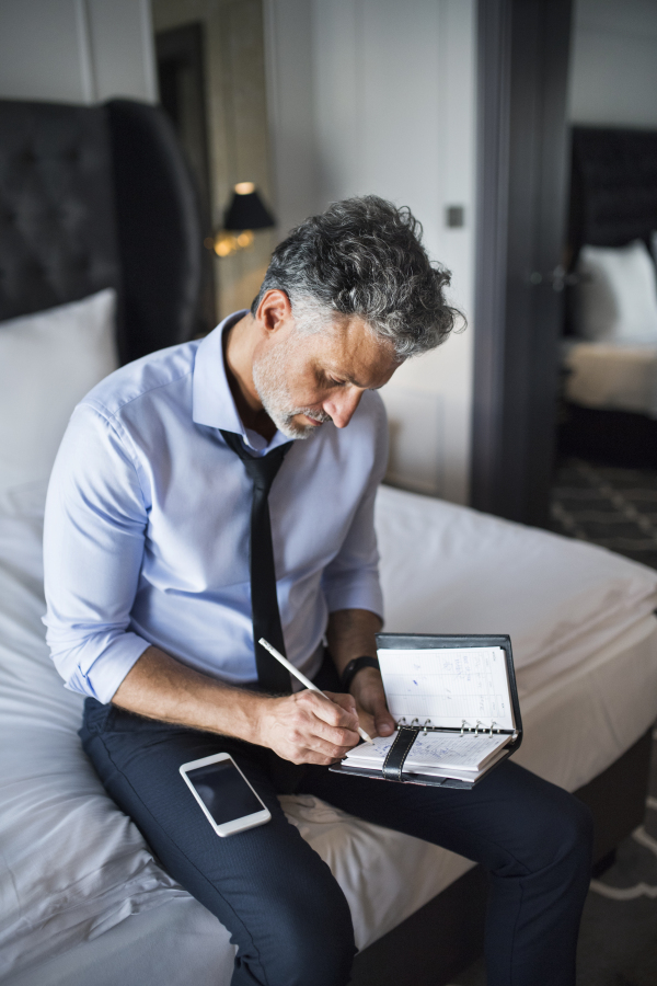 Mature businessman with a smartphone in a hotel room. Handsome man making notes in a diary.