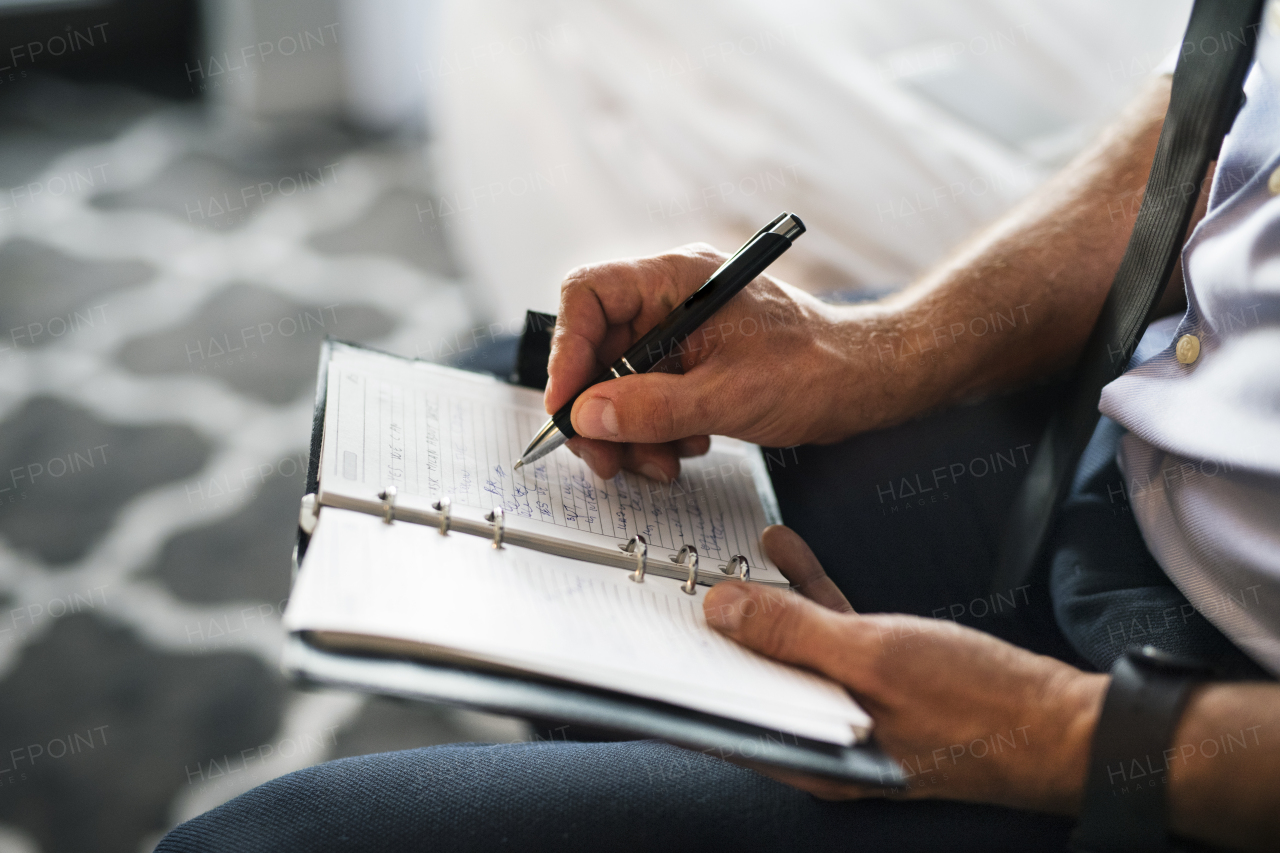 Unrecognizable businessman in a hotel room. Man making notes in a diary. Close up.