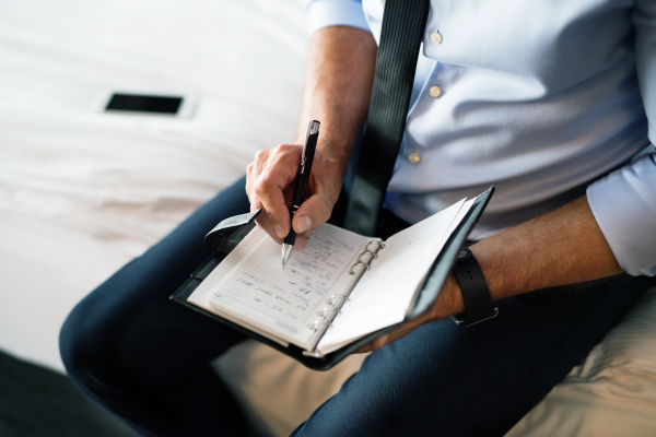 Unrecognizable businessman in a hotel room. Man making notes in a diary. Close up.