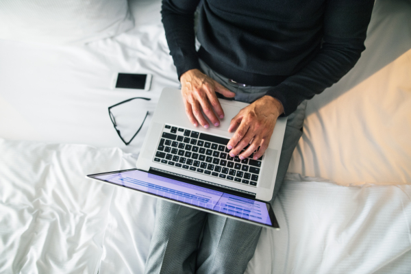 Mature businessman with laptop and smartphone in a hotel room. Unrecognizable man working on a computer.