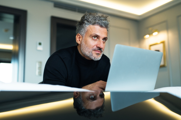 Mature businessman with laptop in a hotel room. Handsome man working on computer.