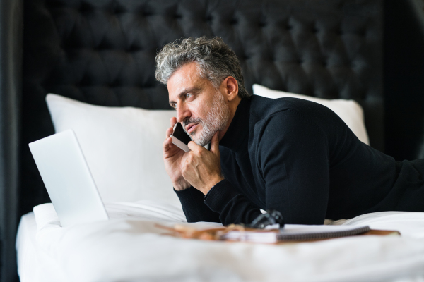 Mature businessman with smartphone in a hotel room. Handsome man making a phone call.