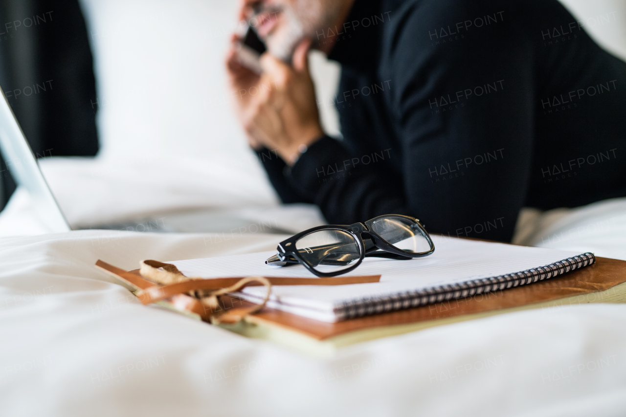 Mature businessman with laptop and smartphone in a hotel room. Unrecognizable man making a phone call.