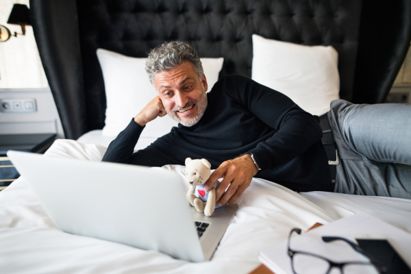 Mature businessman with laptop in a hotel room. Handsome man using online phone call and video.