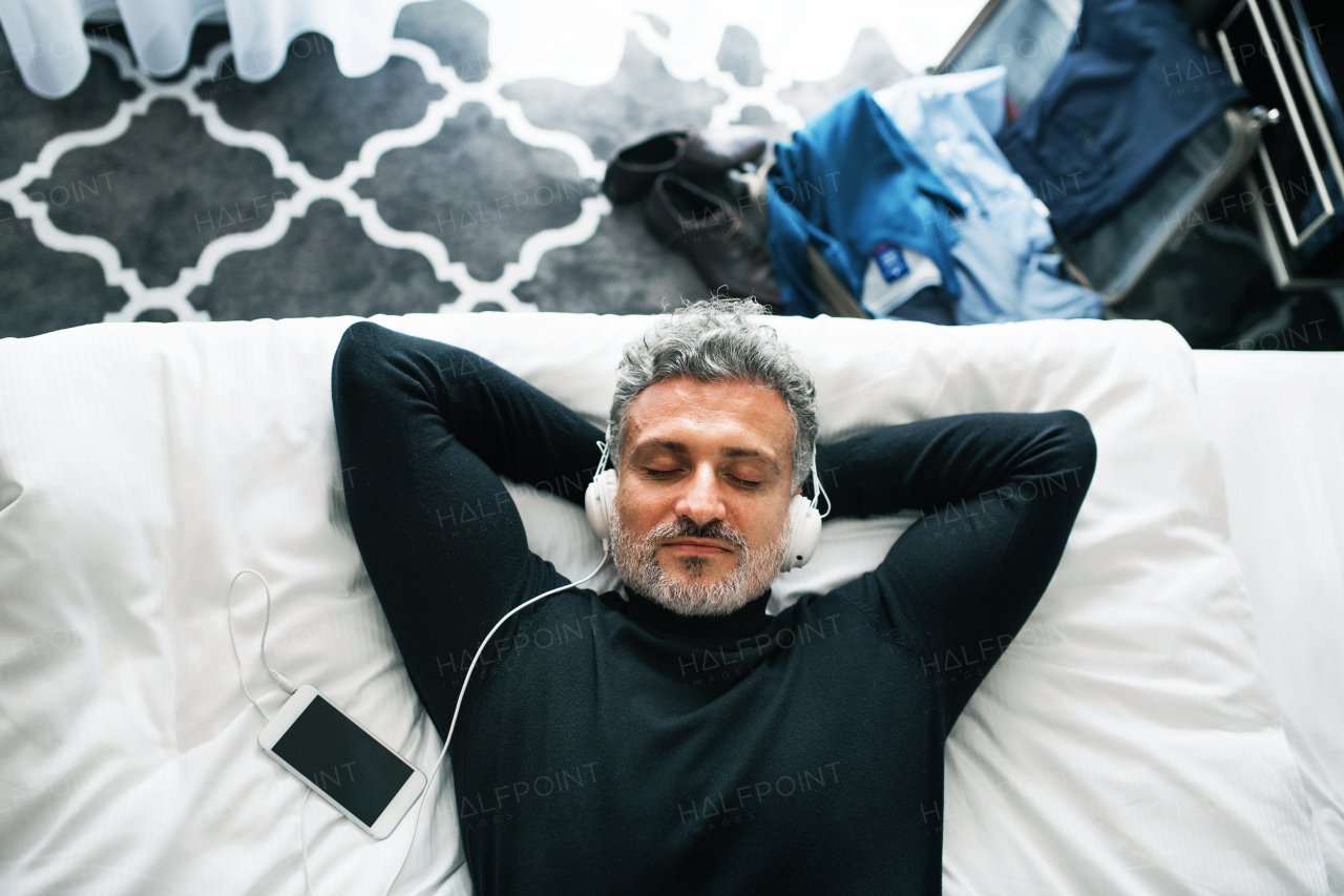 Mature businessman with a smartphone in a hotel room. Handsome man with headphones listening to music.