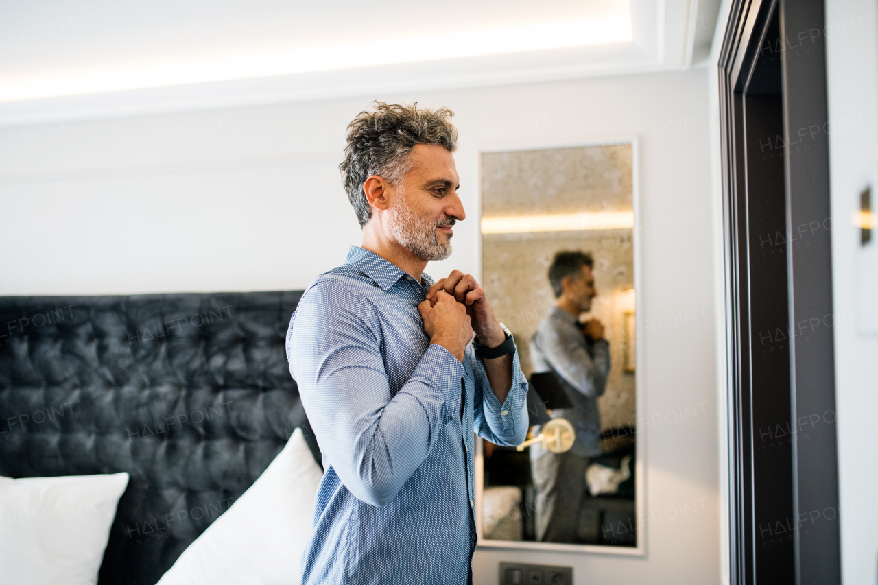 Mature businessman dressing up in a hotel room. Handsome man putting on a shirt.