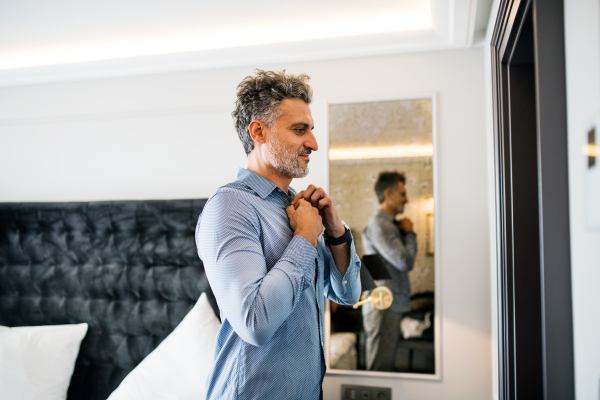 Mature businessman dressing up in a hotel room. Handsome man putting on a shirt.