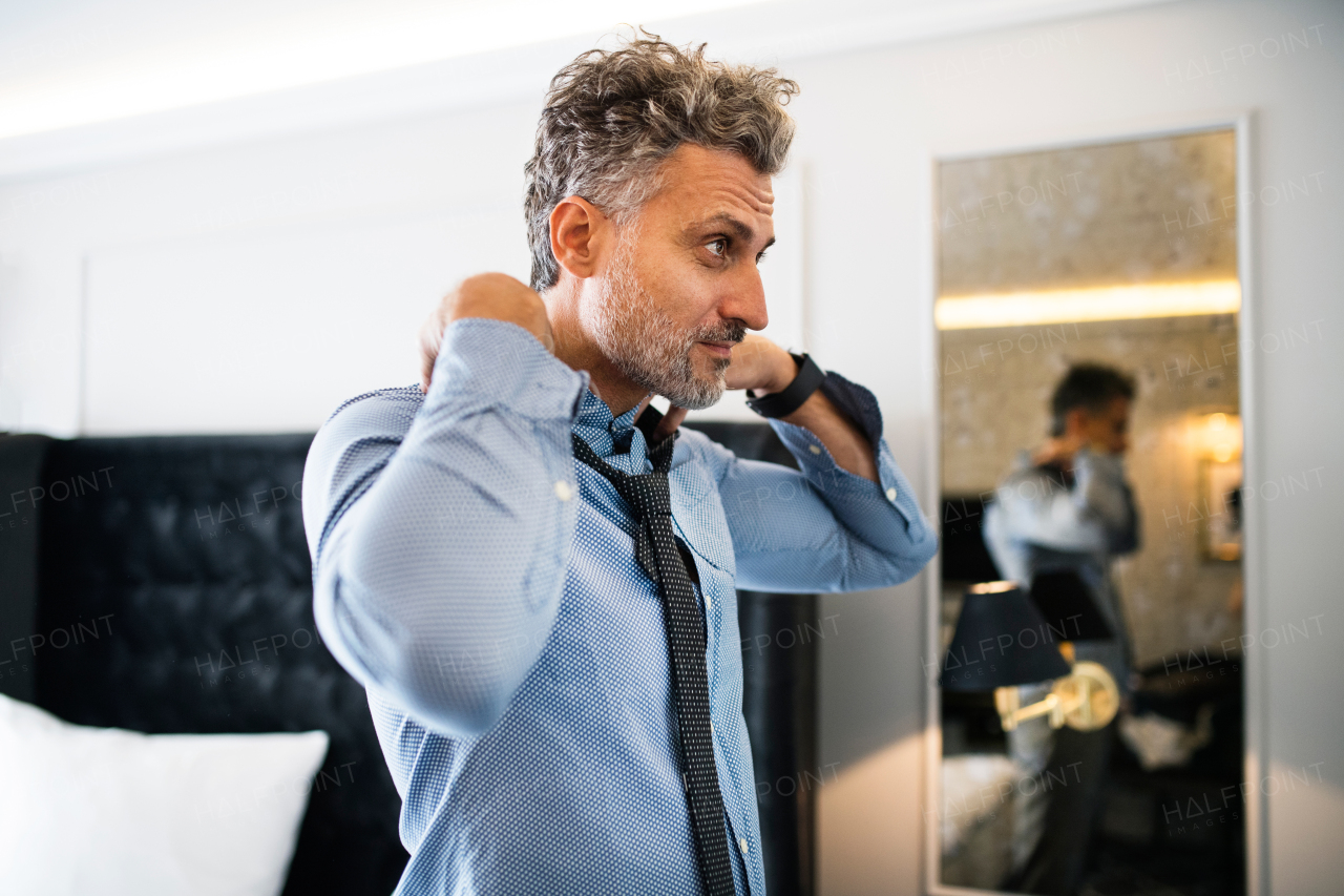 Mature businessman dressing up in a hotel room. Handsome man putting on a tie.