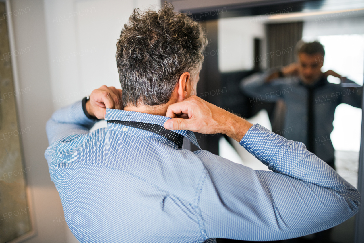 Mature businessman dressing up in a hotel room. Handsome man putting on a tie.