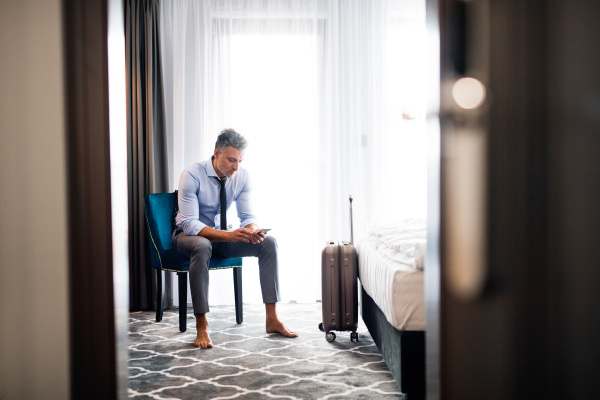 Mature businessman with a smartphone in a hotel room. Handsome man texting.