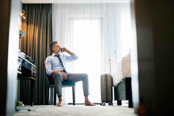 Mature businessman with smartphone in a hotel room. Handsome man sitting on a chair, making a phone call.