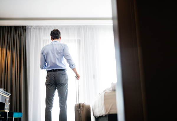 Mature businessman with a smartphone in a hotel room. Handsome man texting. Rear view.