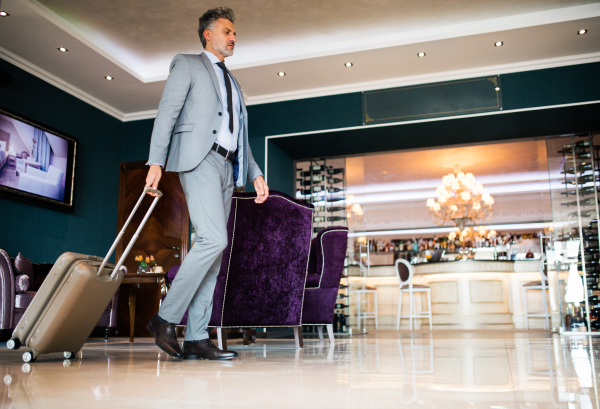 Mature businessman entering or leaving hotel with luggage. Man walking in the hotel entrance hall.