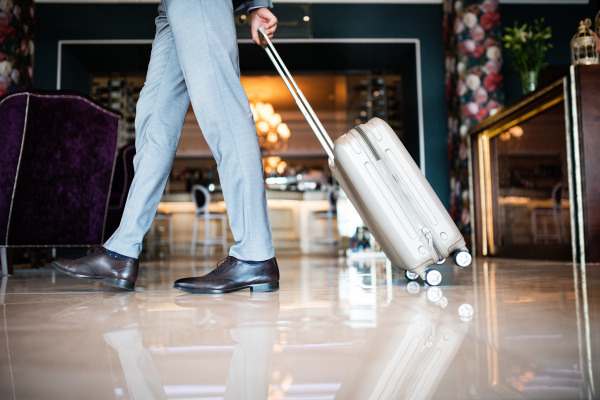 Unrecognizable businessman entering or leaving a hotel with luggage. Man walking in the hotel entrance hall.