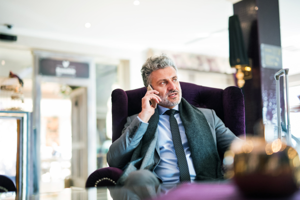 Mature businessman with smartphone in a hotel lounge. Man sitting in a bar or a cafe, making a phone call.