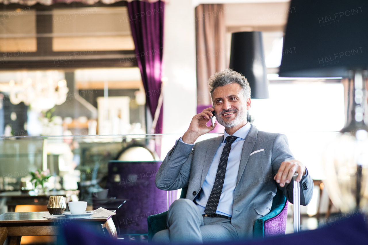 Handsome mature businessman with smartphone in a hotel lounge, making a phone call.