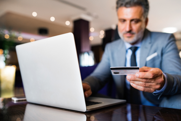 Handsome mature businessman with laptop in a hotel lounge. Man holding a credit card. Internet banking. Online payment.