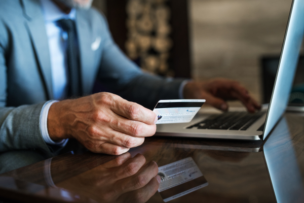 Unrecognizable mature businessman with laptop in a hotel lounge. Man holding a credit card. Internet banking. Online payment.