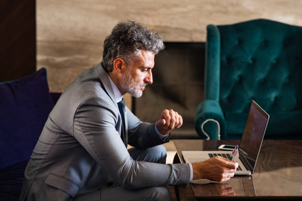 Handsome mature businessman with laptop in a hotel lounge. Man holding a credit card. Internet banking. Online payment.