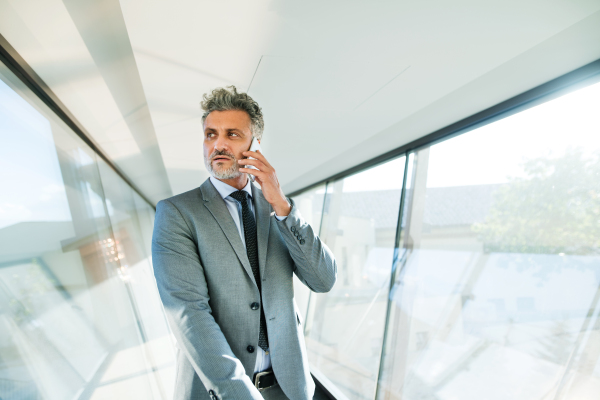 Mature businessman with smartphone walking in the corridor, travelling.