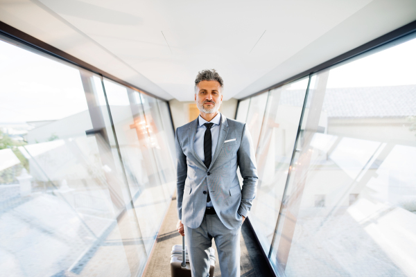 Mature businessman walking in the corridor with suitcase, travelling.