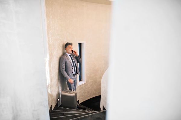 Mature businessman with smartphone leaning on a concrete wall, making a phone call.