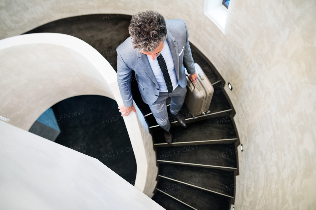 Mature businessman with suitcase walking down the stairs, travelling. Top view.