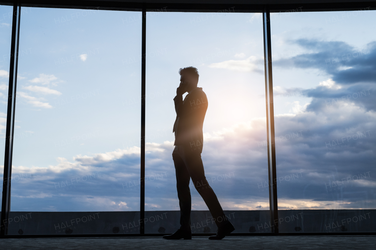 Mature businessman in a hotel with a smartphone. Man making a phone call, walking along big windows.