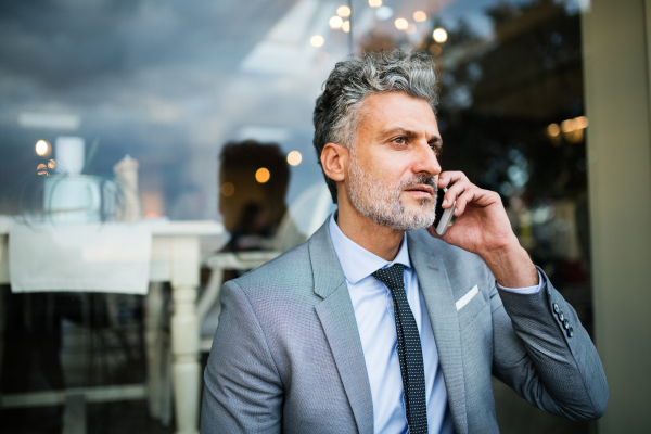 Mature businessman with smartphone standing in an outdoor hotel cafe. Man making a phone call.