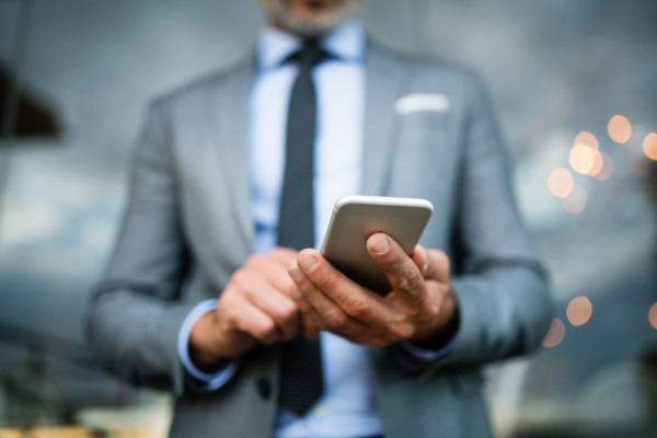 Unrecognizable businessman with smartphone standing in an outdoor hotel cafe. Man text messaging.