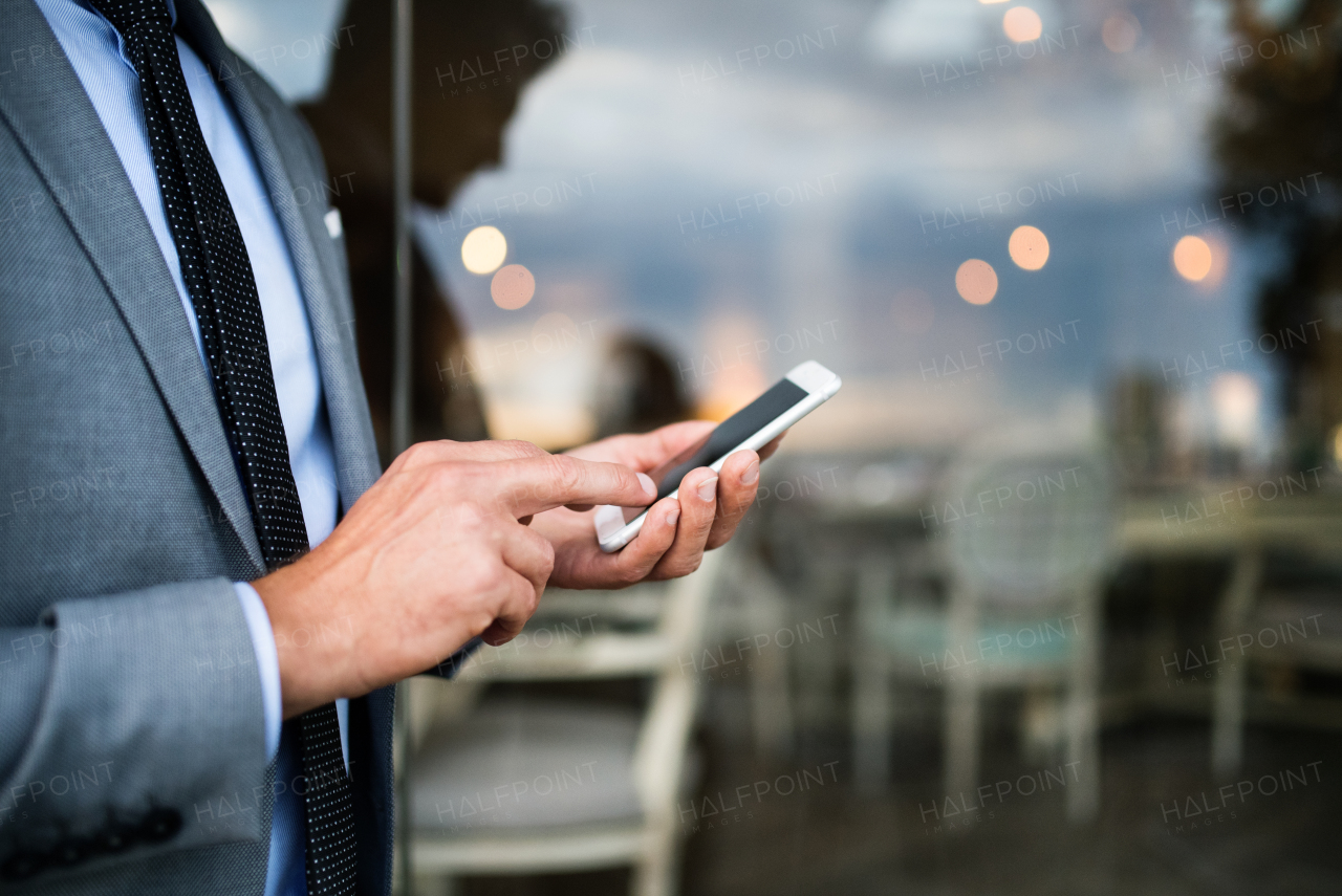 Unrecognizable businessman with smartphone standing in an outdoor hotel cafe. Man text messaging.