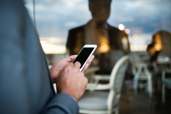 Unrecognizable businessman with smartphone standing in an outdoor hotel cafe. Man text messaging.