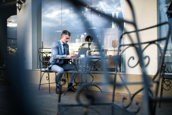 Mature businessman with laptop sitting in an outdoor hotel cafe.