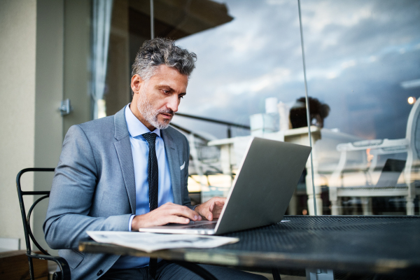 Mature businessman with laptop sitting in an outdoor hotel cafe.