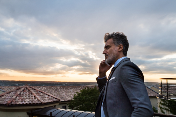 Mature businessman in a hotel balcony with a smartphone. Man making a phone call.