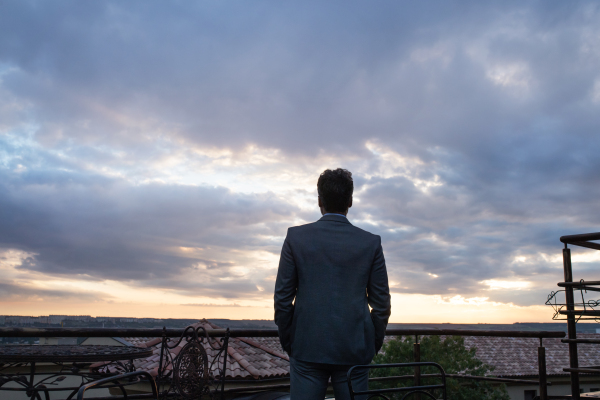 Mature businessman standing in a hotel balcony in the evening. Rear view.