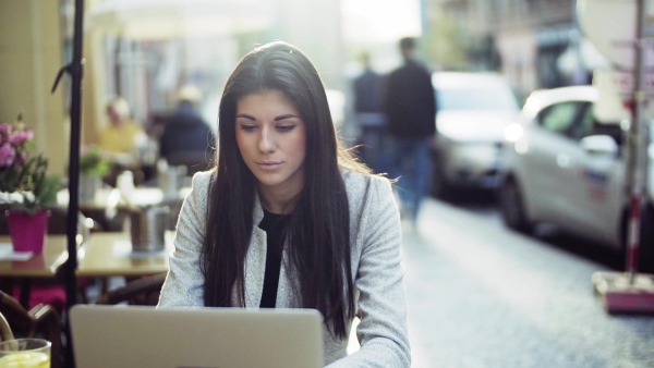 Young attractive business woman with laptop sitting in a cafe in city, working. Slow motion.