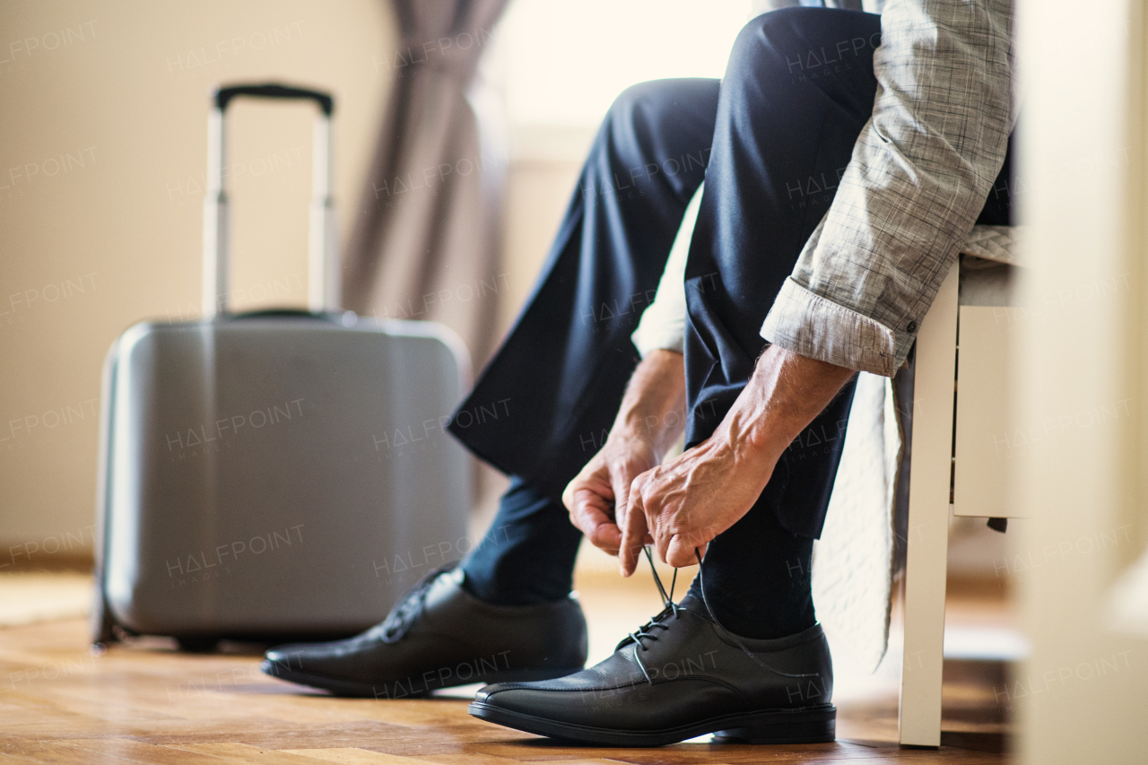 Midsection view of unrecognizable mature businessman on a business trip sitting ina hotel room, tying shoelaces.