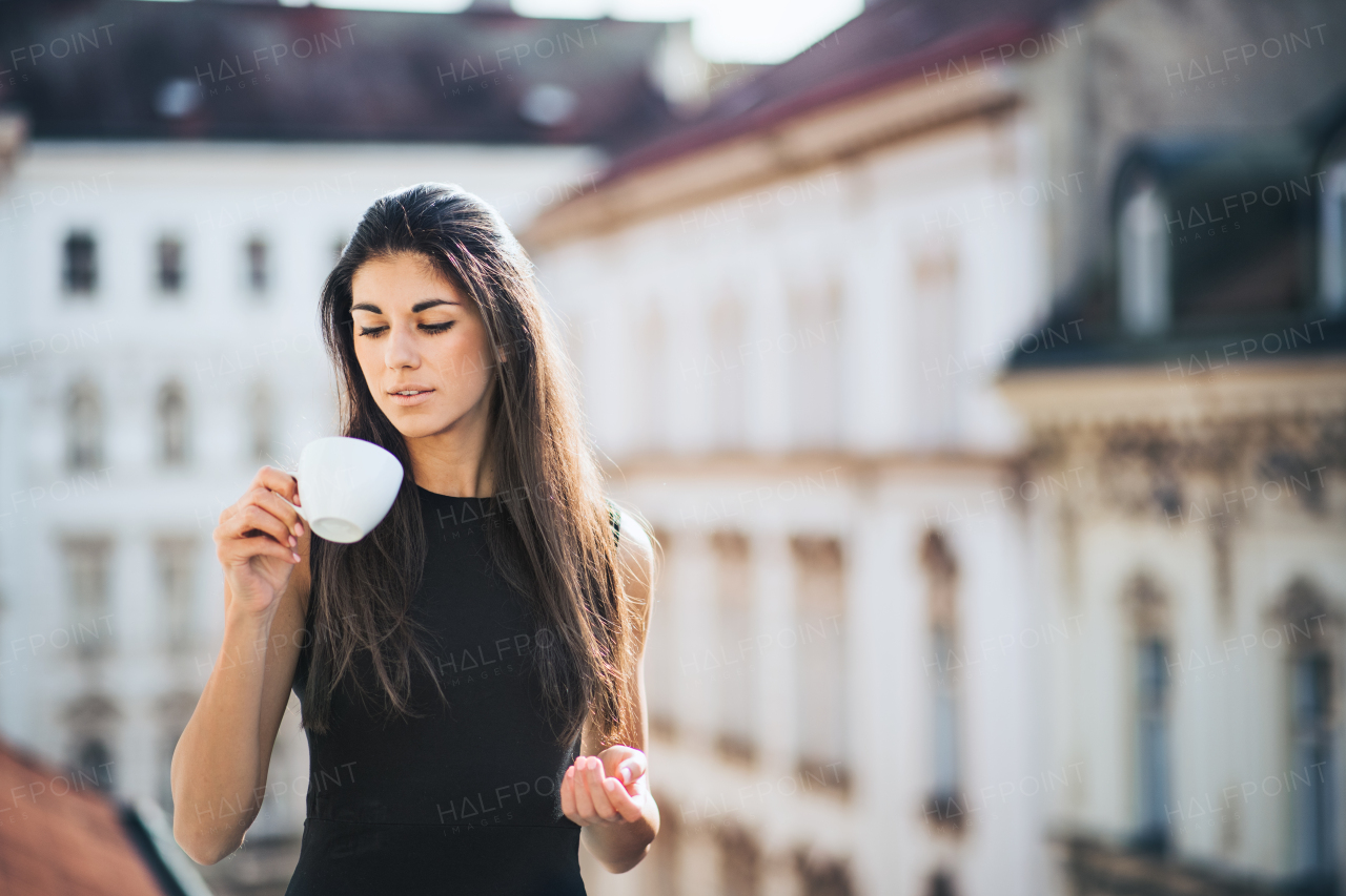 Happy young businesswoman with cup of coffee standing on a terrace outside an office in city. Copy space.