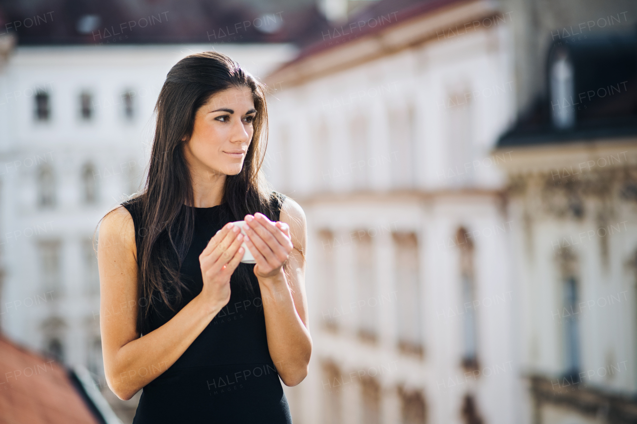 Happy young businesswoman with cup of coffee standing on a terrace outside an office in city. Copy space.