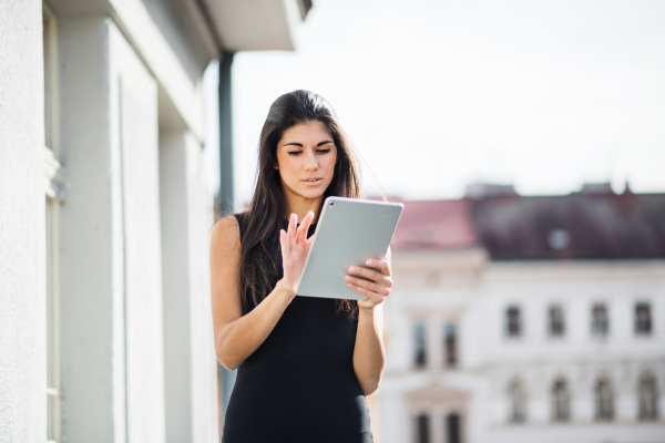 Young businesswoman with tablet standing on a terrace outside an office in city. Copy space.