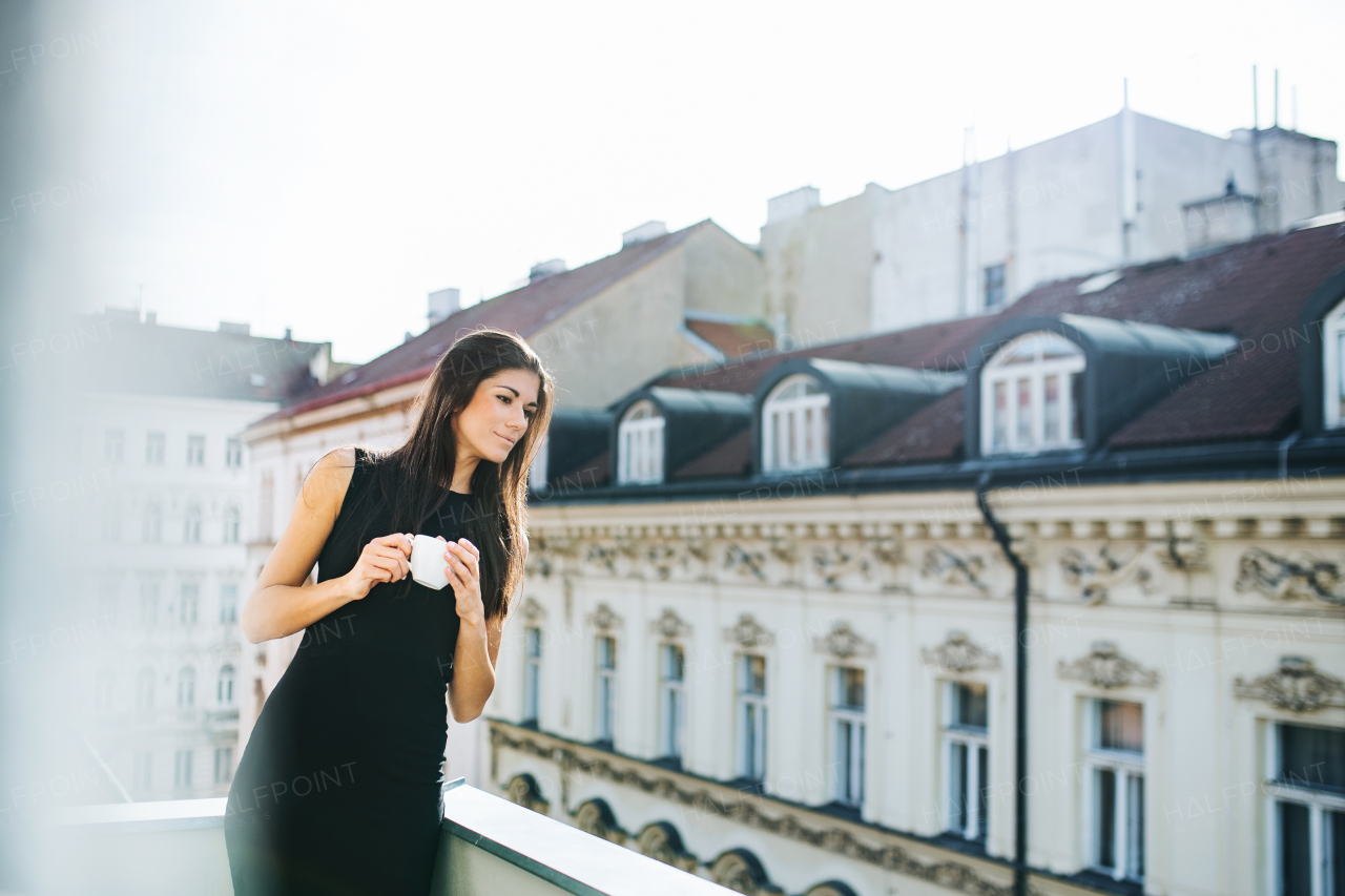 Happy young businesswoman with cup of coffee standing on a terrace outside an office in city. Copy space.