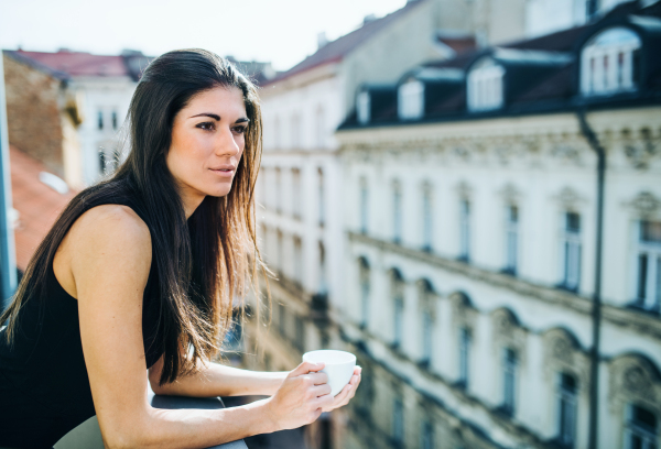 Happy young businesswoman with cup of coffee standing on a terrace in an office in city. Copy space.