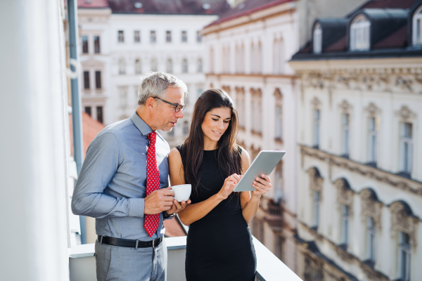 Man and woman business partners with tablet standing on a terrace in office in city, talking.