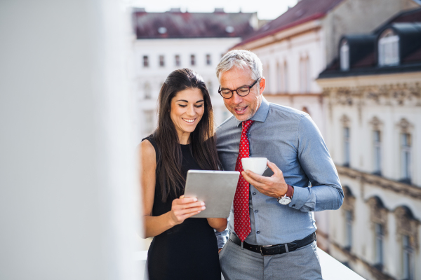 Man and woman business partners with tablet standing on a terrace in office in city, talking.