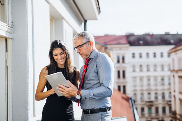 Man and woman business partners with tablet standing on a terrace in office in city, talking.