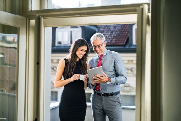 Man and woman business partners with tablet and coffee standing on a terrace in office in city, talking.